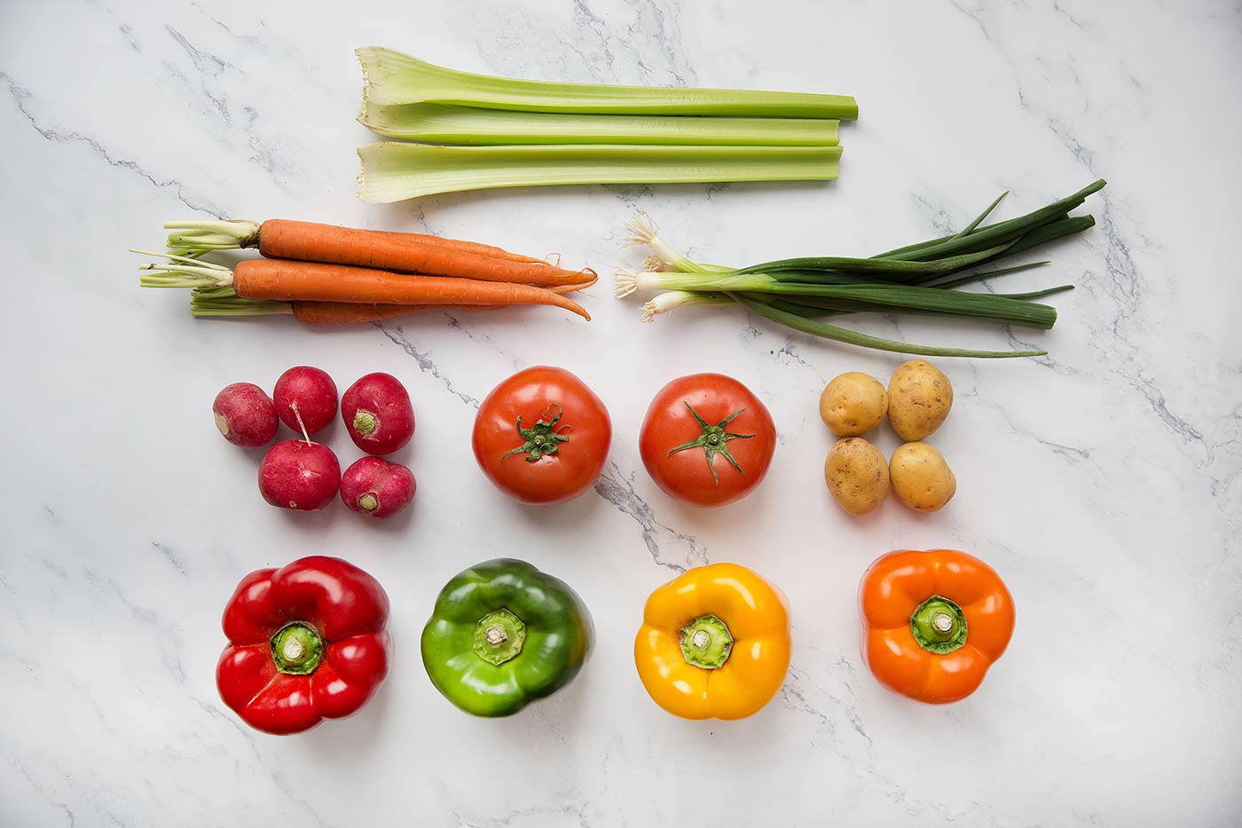 Marble surface with red, green, yellow & orange peppers, tomatoes, potatoes, radishes, carrots, spring onions & celery